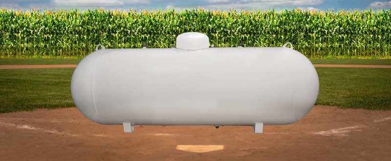 Horizontal Propane tank on a baseball diamond by a cornfield.